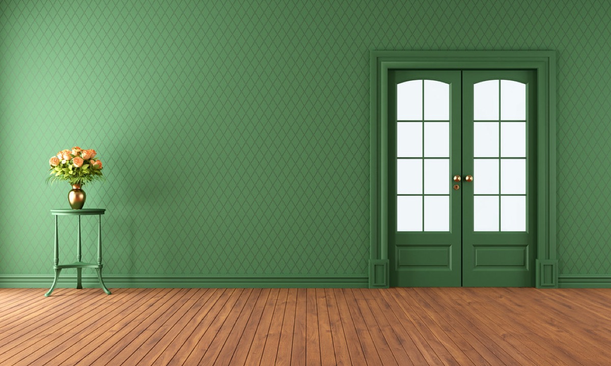 An empty living room with a polished wood floor and a vase of roses on a side table